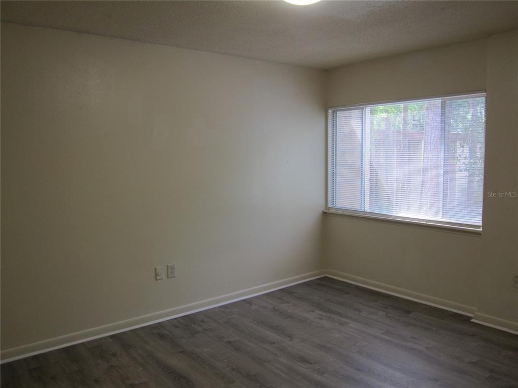 An empty room features light-colored walls, gray wood-look flooring, and a window with blinds — 300 NW 20TH AVENUE UNIT 6, GAINESVILLE, FL