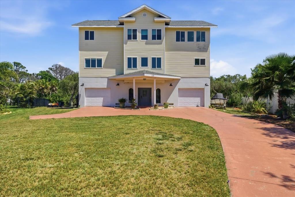 A three-story house with light yellow siding, a red driveway, and two garage doors — 1130 S FLORIDA AVENUE, TARPON SPRINGS, FL