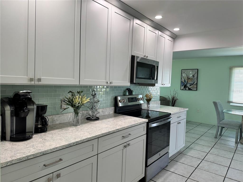 A kitchen features white shaker cabinets, light countertops, a glass tile backsplash, and stainless appliances — 1048 PORPOISE ROAD, VENICE, FL
