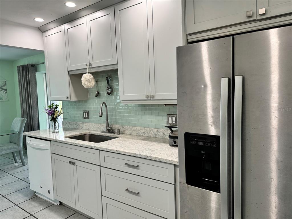 A kitchen features light gray cabinets, a light green tile backsplash, and stainless steel appliances — 1048 PORPOISE ROAD, VENICE, FL
