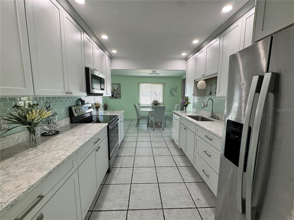 A galley kitchen features white cabinets, light countertops, a subway tile backsplash, and tile flooring — 1048 PORPOISE ROAD, VENICE, FL