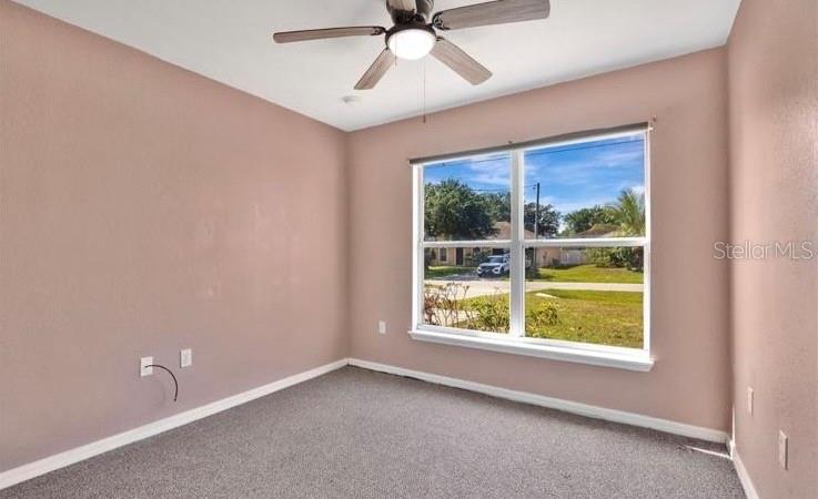 An empty bedroom features light-colored walls, gray carpeting, a ceiling fan, and a large window — 50 SAWFISH COURT, KISSIMMEE, FL