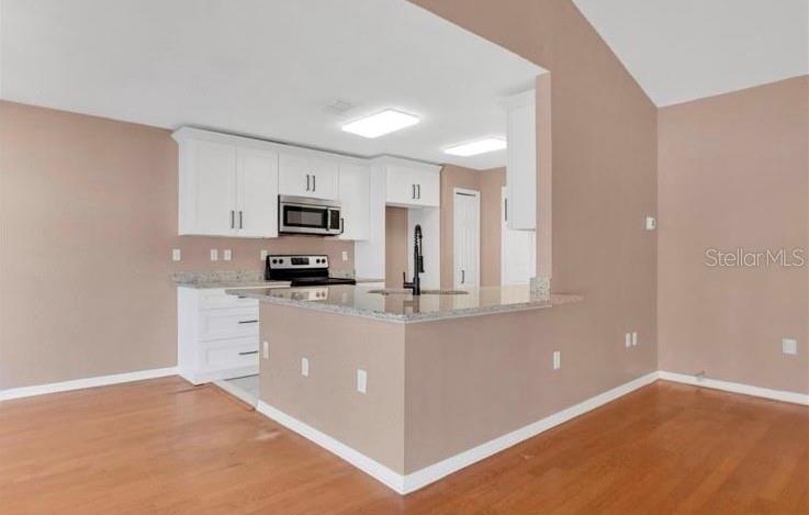 A kitchen with white cabinets, stainless steel appliances, and a granite-topped peninsula island — 50 SAWFISH COURT, KISSIMMEE, FL