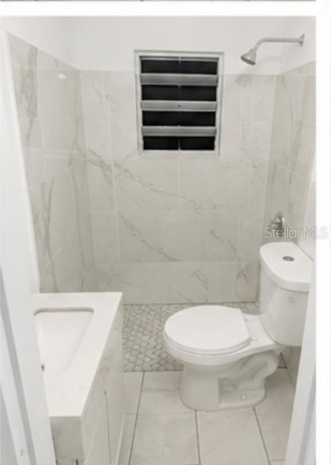 A small bathroom features a white toilet, a vanity sink, and light-colored marble-patterned wall tiles — 122 BADE PEREZ ST., GUAYAMA, PR