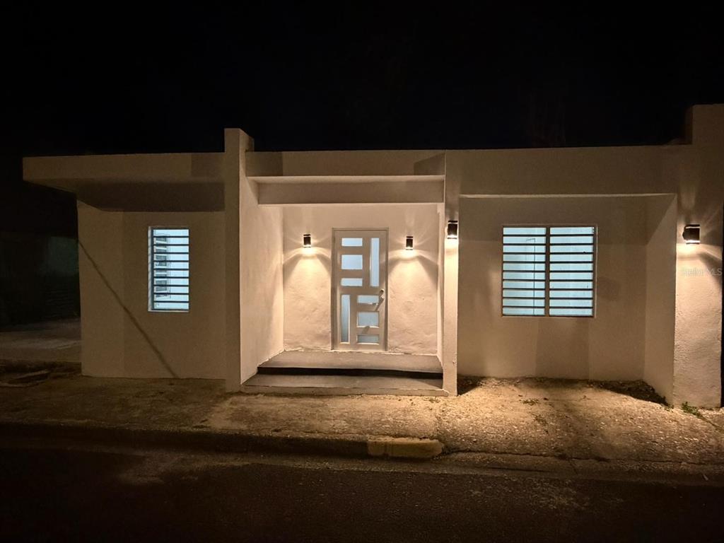 A white, single-story house exterior at night with a central entrance and louvered windows — 122 BADE PEREZ ST., GUAYAMA, PR