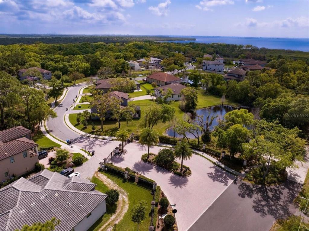 An aerial view shows a gated residential neighborhood with houses, a pond, and distant water — 7849 MARSH POINTE DRIVE, TAMPA, FL