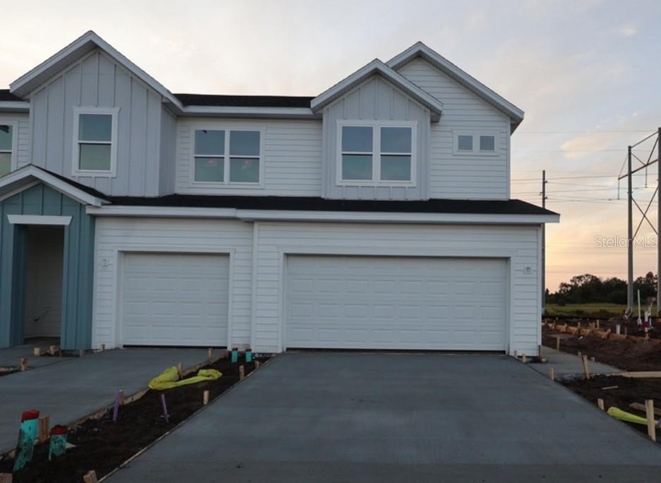 A two-story duplex with white siding, two garage doors, and a concrete driveway at dusk — 6418 JENSEN VIEW AVENUE, APOLLO BEACH, FL