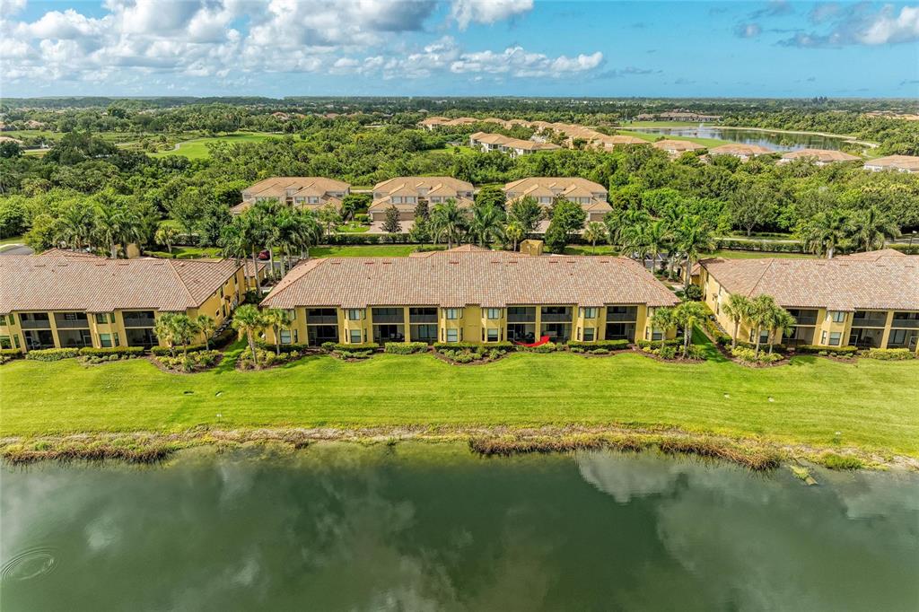 An aerial view shows multi-story apartment buildings with tiled roofs situated beside a large pond — 7305 RIVER HAMMOCK DRIVE UNIT 102, BRADENTON, FL