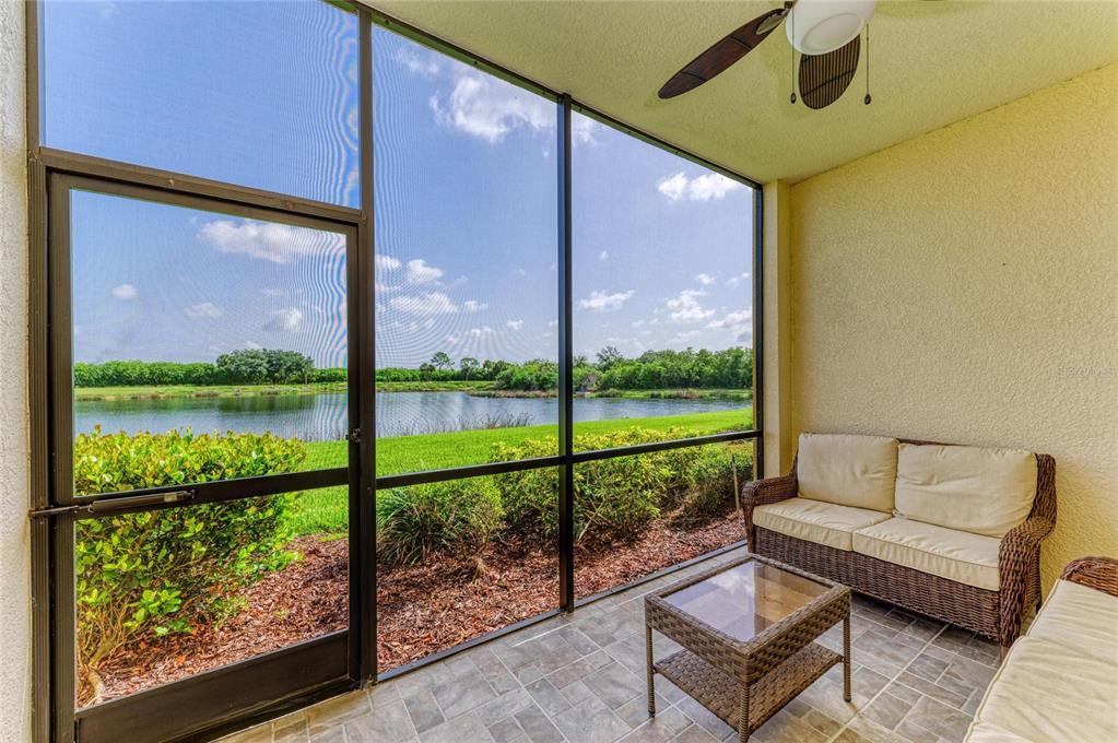 A screened-in patio features wicker furniture, tile flooring, and a view of a pond — 7305 RIVER HAMMOCK DRIVE UNIT 102, BRADENTON, FL