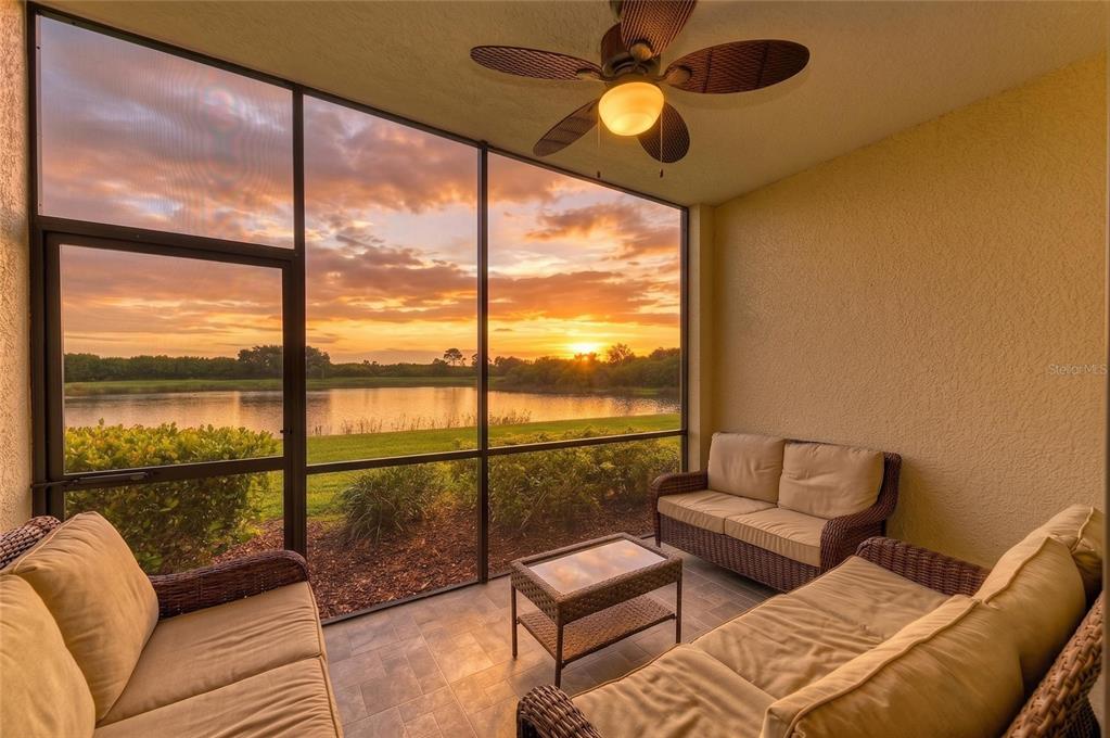 A screened-in patio with wicker furniture overlooks a lake during a sunset — 7305 RIVER HAMMOCK DRIVE UNIT 102, BRADENTON, FL