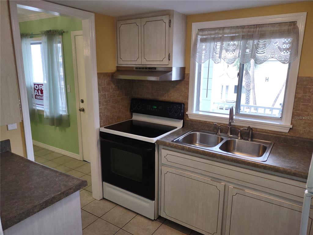 A kitchen features a black electric range, a double-basin sink, and light-colored cabinetry — 1566 PLEASANT ROAD UNIT J24, BRADENTON, FL