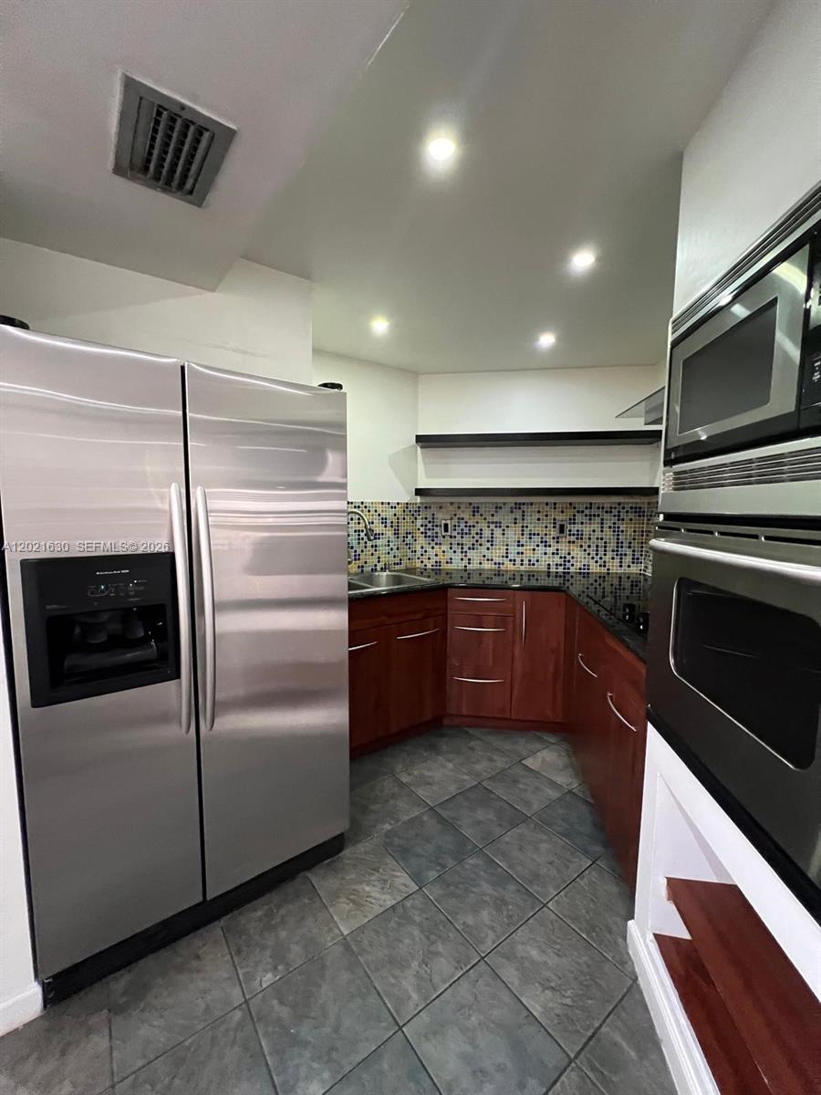 A kitchen features stainless steel appliances, dark wood cabinets, a mosaic backsplash, and tile flooring — 9715 Fontainebleau Blvd # E308, Miami FL 33172, MIAMI, FL