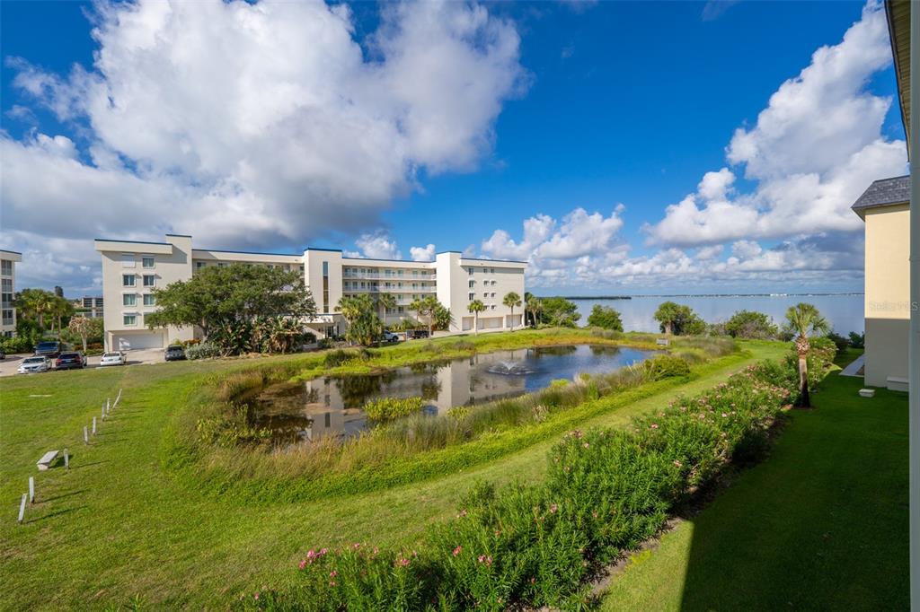 An exterior view of a multi-story apartment building overlooking a pond and a large body of water — 190 ESCAMBIA LANE UNIT 305, COCOA BEACH, FL