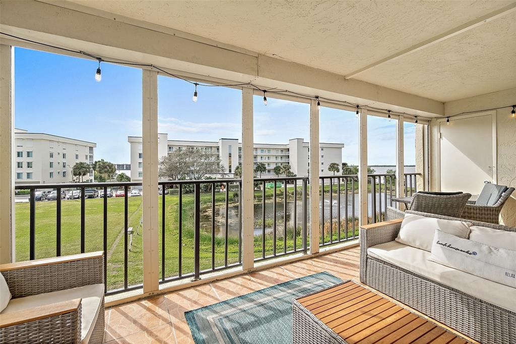A screened-in balcony features wicker furniture, a tiled floor, and views of a pond — 190 ESCAMBIA LANE UNIT 305, COCOA BEACH, FL