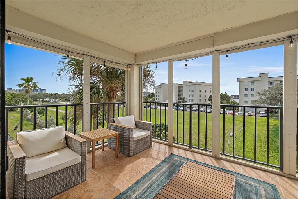 A screened-in balcony with tiled flooring, wicker chairs, and a view of a grassy lawn — 190 ESCAMBIA LANE UNIT 305, COCOA BEACH, FL