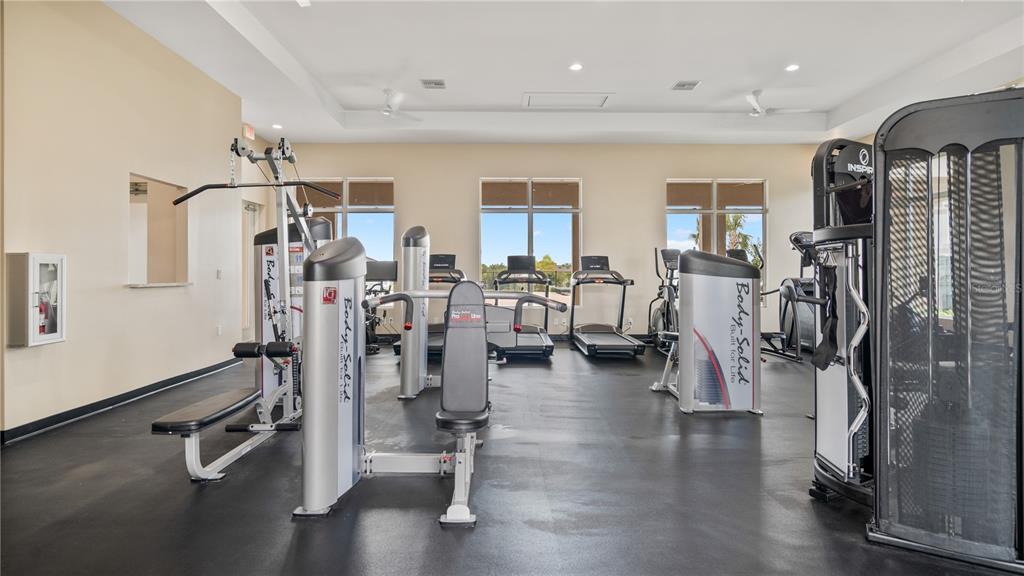 A gym room features black rubber flooring, multiple exercise machines, and large windows — 2496 BEVEL LANE, DAVENPORT, FL