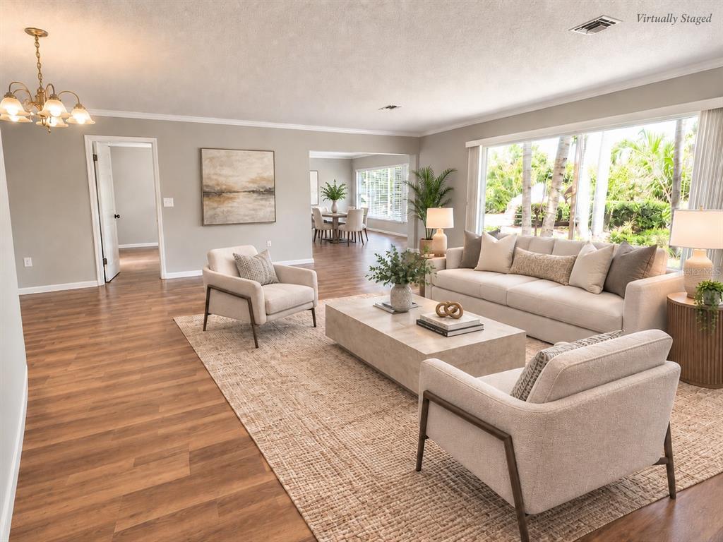 A living room with wood-look flooring, a beige sofa, two armchairs, and a large window — 7708 2ND AVENUE W, BRADENTON, FL
