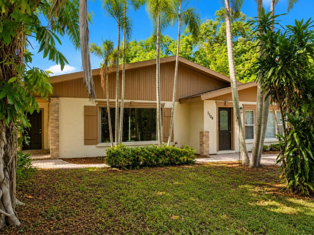 A single-story house with a beige stucco exterior, brown trim, and palm trees in the yard — 7708 2ND AVENUE W, BRADENTON, FL