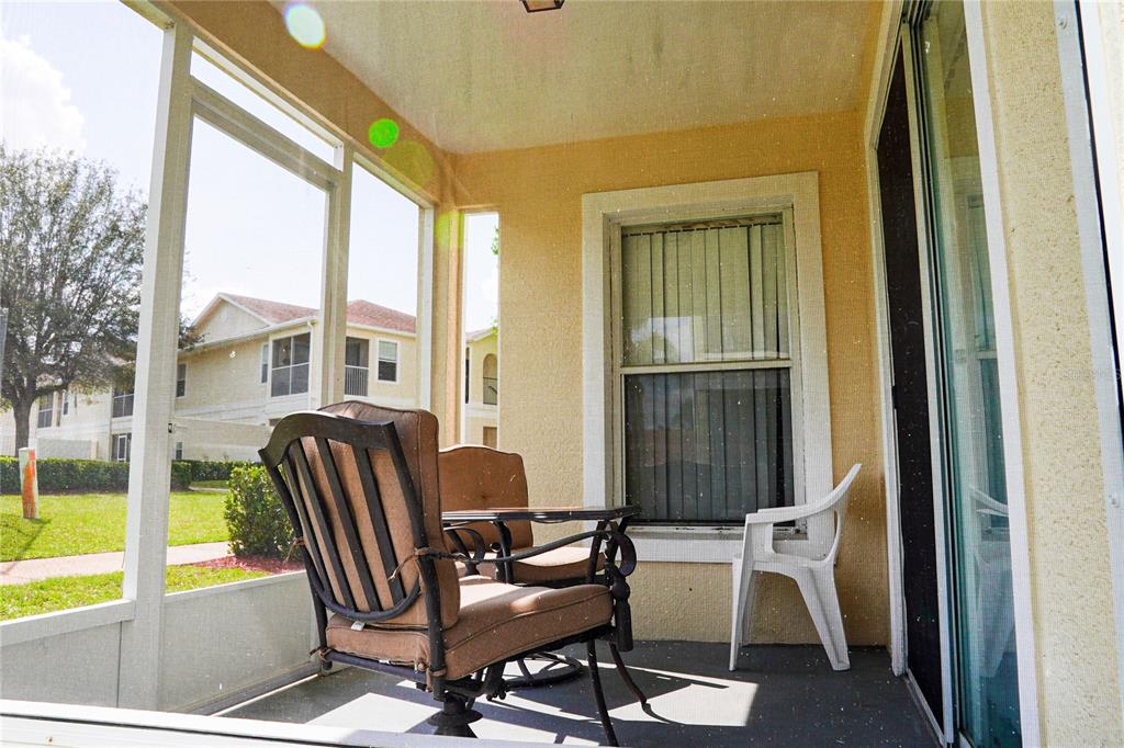 A screened-in patio features two cushioned chairs, a small table, and a white plastic chair — 8812 GRAND PALMS CIRCLE UNIT A, KISSIMMEE, FL