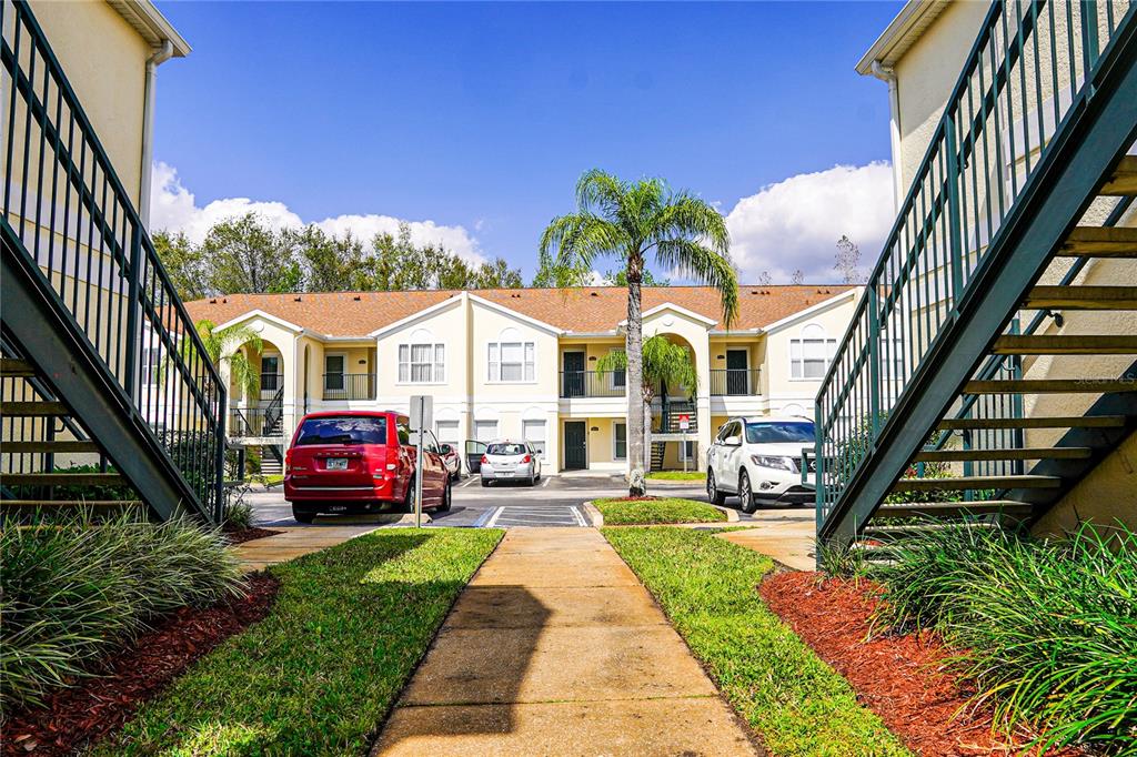 A paved walkway leads between two staircases toward a two-story apartment building with parked cars — 8812 GRAND PALMS CIRCLE UNIT A, KISSIMMEE, FL