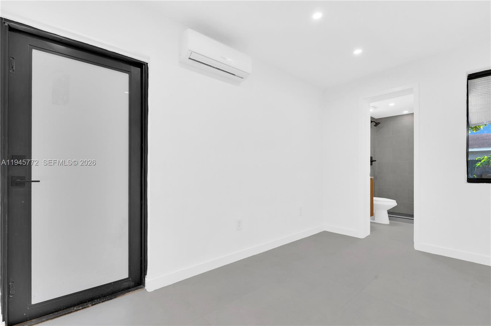 A minimalist room features white walls, gray tile flooring, a glass door, and an attached bathroom — 3040 NW 93rd St # A, Miami FL 33147, MIAMI, FL