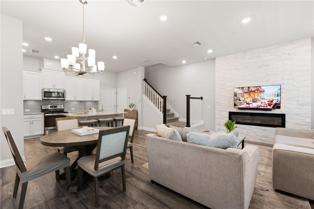 An open-concept living room and kitchen featuring a white stone fireplace and wood-look flooring — 934 WILD DATE LANE, LAKE MARY, FL