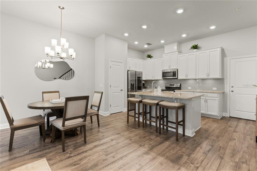 A kitchen and dining area with white cabinets, a granite island, and wood-look flooring — 934 WILD DATE LANE, LAKE MARY, FL