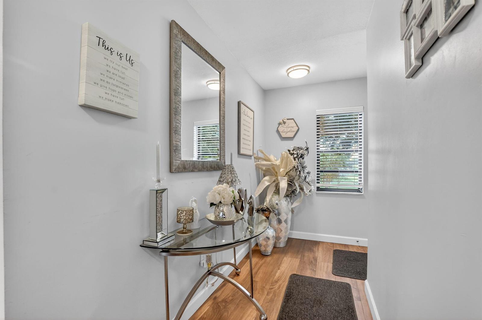 A hallway features a glass console table, a wall mirror, and wood-look flooring — 21501 Juego Circle # F, Boca Raton FL 33433, BOCA RATON, FL