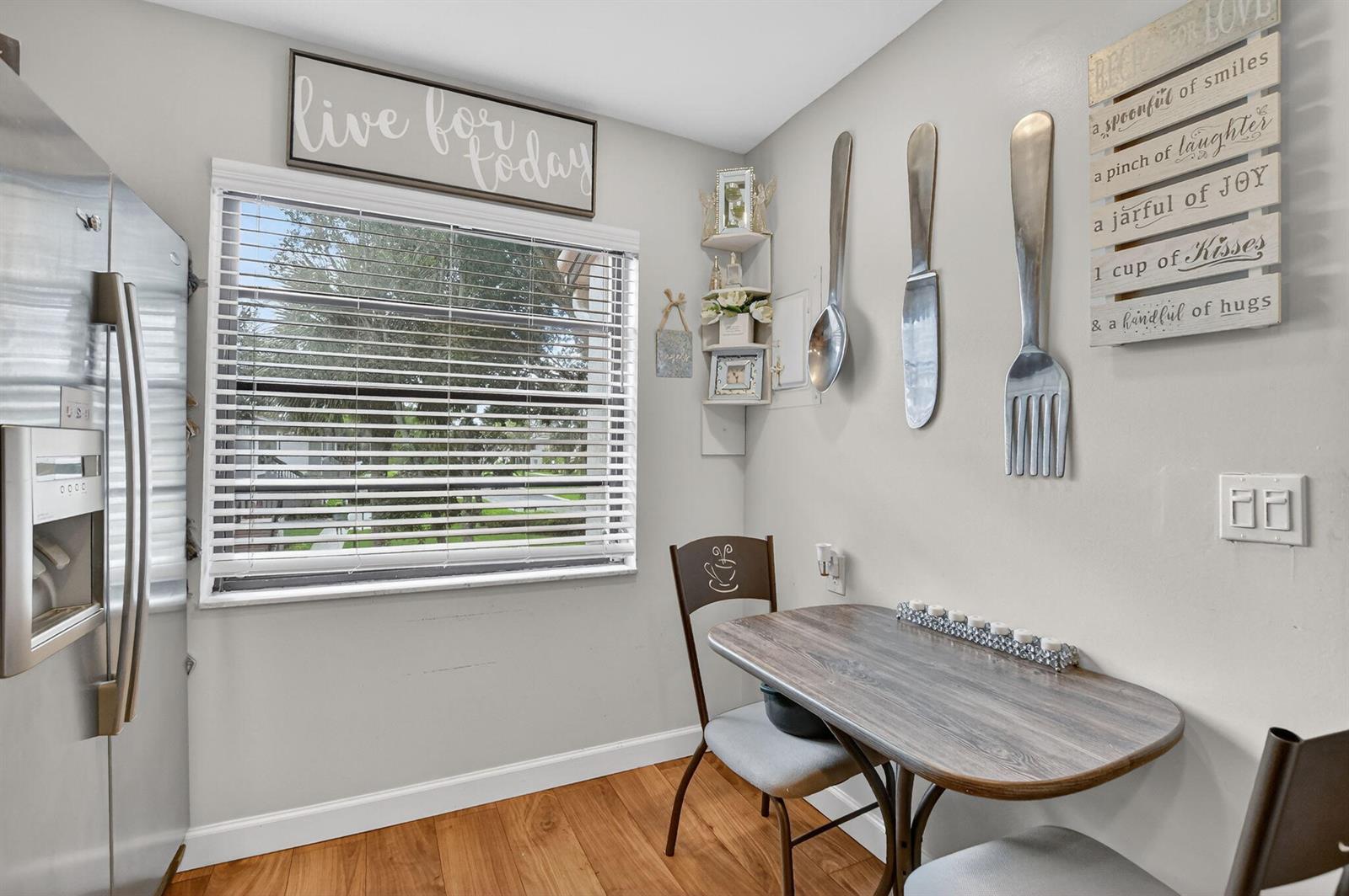 A small kitchen dining area features a window, wooden floors, and oversized wall-mounted utensils — 21501 Juego Circle # F, Boca Raton FL 33433, BOCA RATON, FL