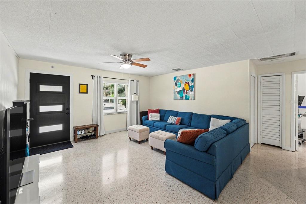 A living room features a blue sectional sofa, a ceiling fan, and light-colored terrazzo flooring — 6251 12TH AVE S, GULFPORT, FL