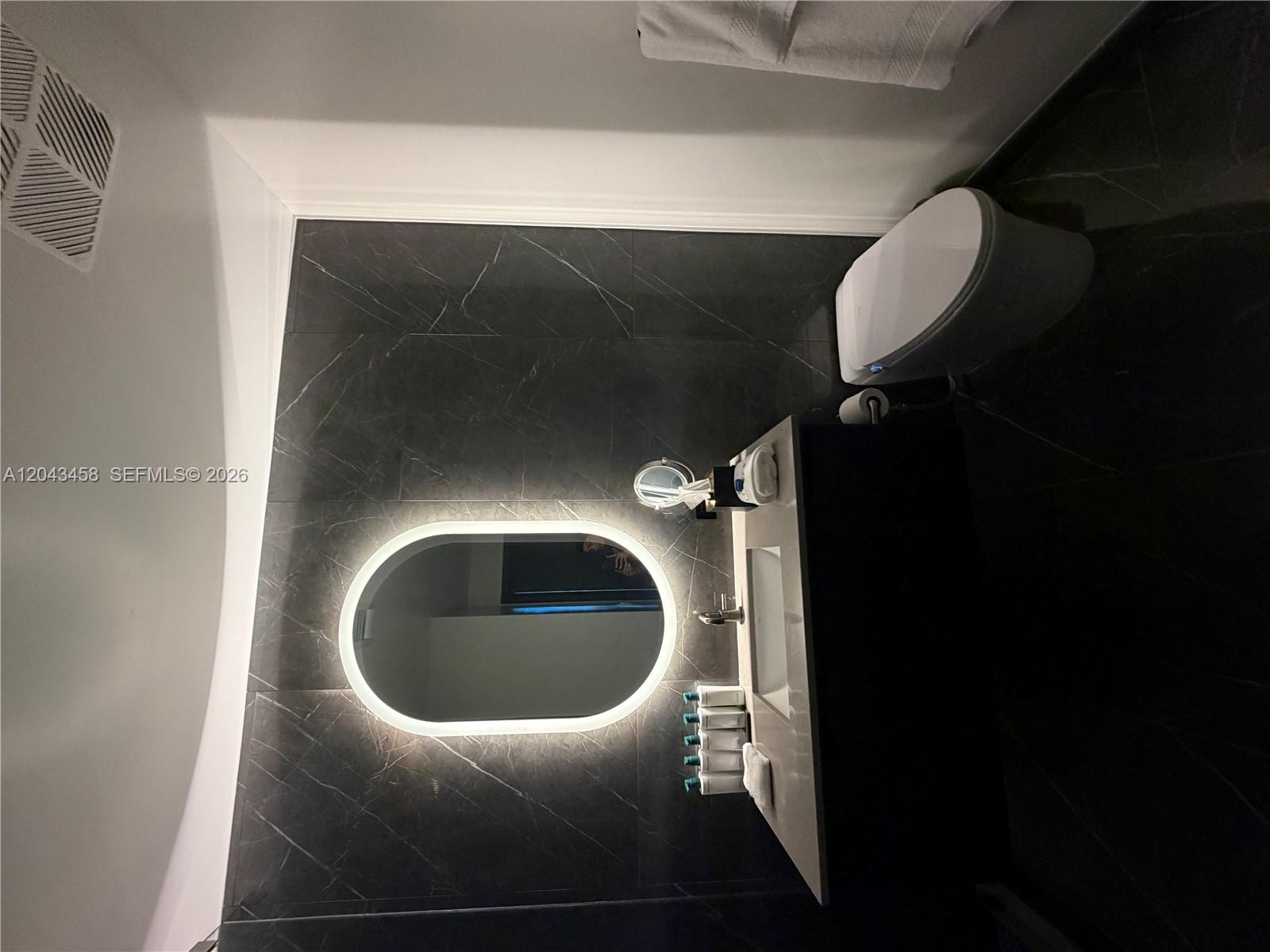 A modern bathroom features dark marble-look tile, a backlit oval mirror, and a white toilet — 20 NE 11th St # 5103, Miami FL 33132, MIAMI, FL