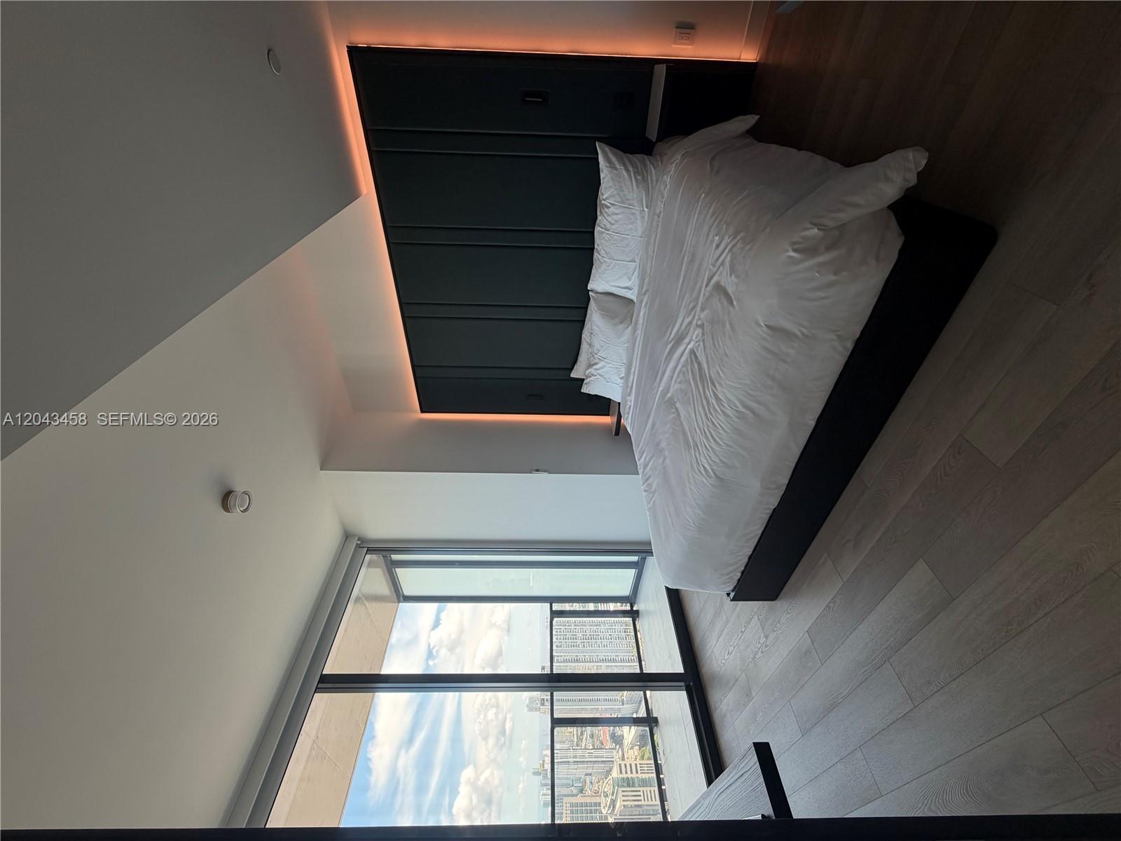 A modern bedroom features a dark paneled headboard with accent lighting and floor-to-ceiling windows — 20 NE 11th St # 5103, Miami FL 33132, MIAMI, FL