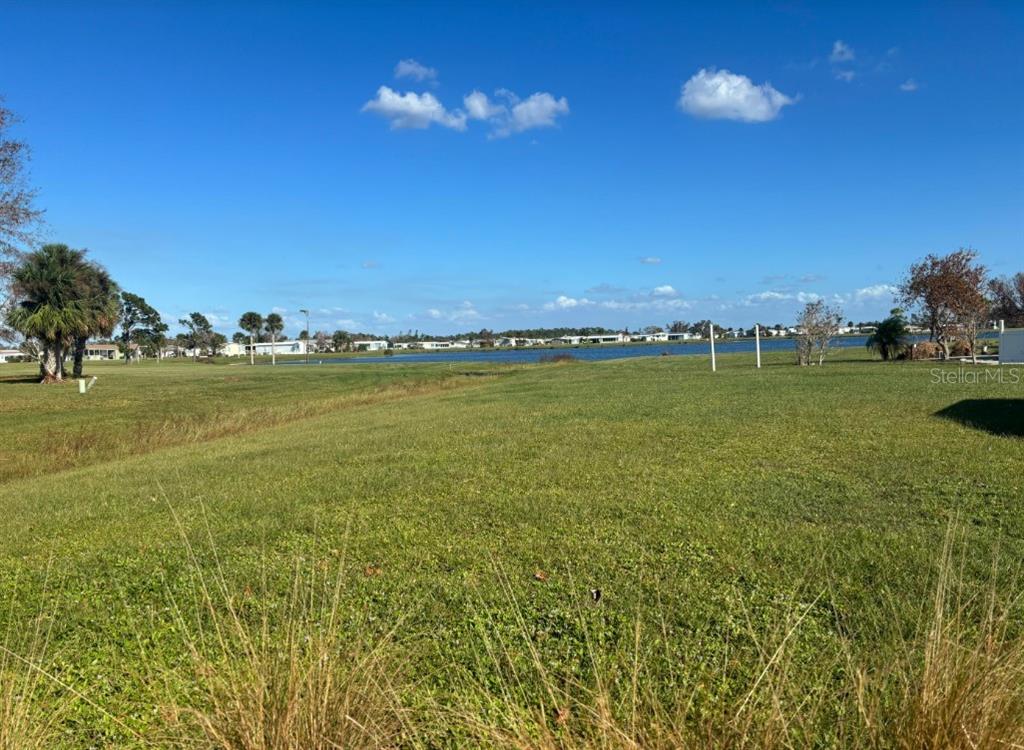A grassy lot overlooks a lake with distant houses under a clear blue sky — 7416 WIDNESS LANE, PORT CHARLOTTE, FL