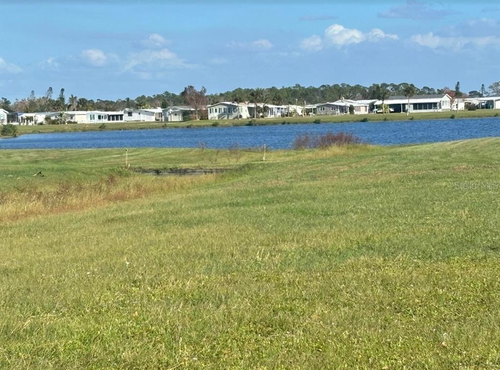 A grassy field overlooks a small lake with a row of houses in the distance — 7416 WIDNESS LANE, PORT CHARLOTTE, FL