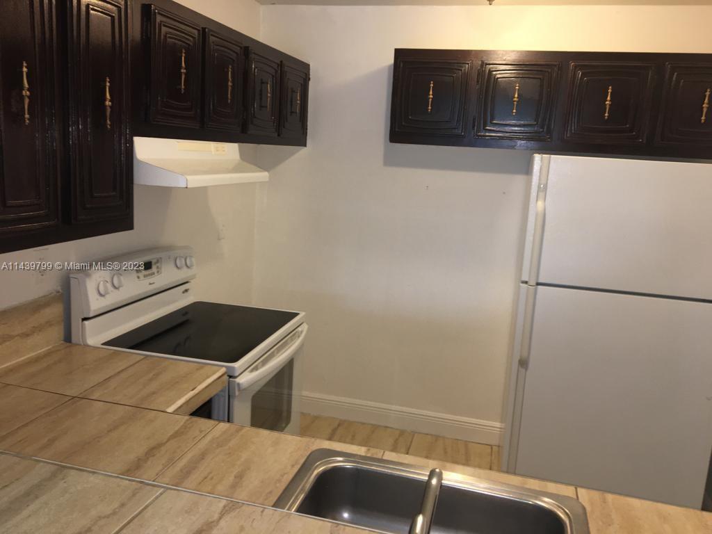 A kitchen features dark wood cabinets, a white stove, a white refrigerator, and tiled countertops — 498 NW 165th St Rd # D205, Miami FL 33169, MIAMI, FL