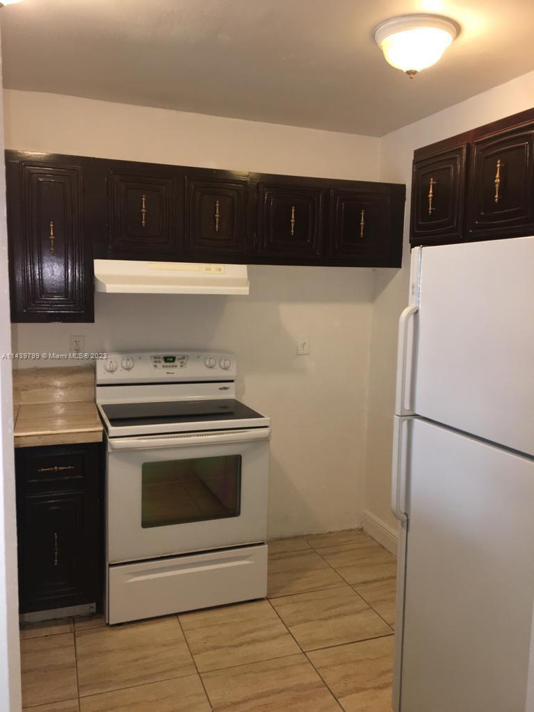 A kitchen features dark wood cabinets, a white stove, and a white refrigerator on tiled floors — 498 NW 165th St Rd # D205, Miami FL 33169, MIAMI, FL