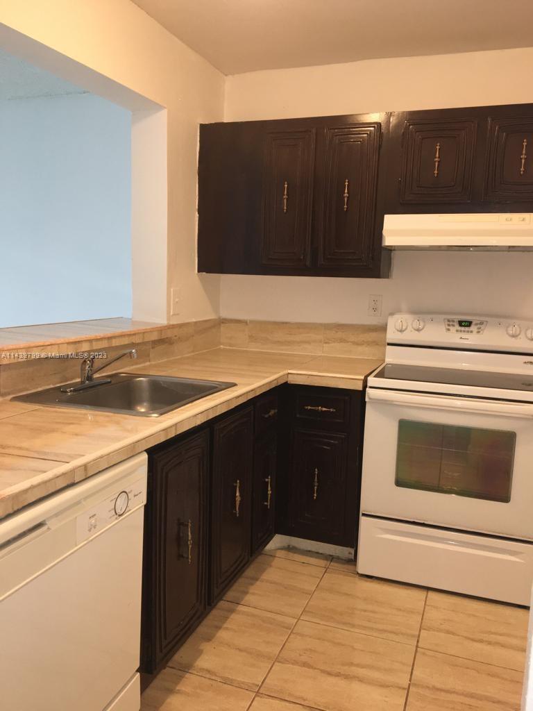 A kitchen features dark wood cabinets, a white stove, a stainless steel sink, and tile flooring — 498 NW 165th St Rd # D205, Miami FL 33169, MIAMI, FL