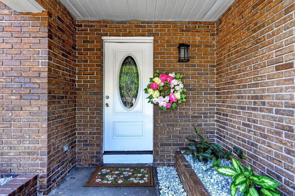 A white front door with an oval glass insert sits in a brown brick entryway — 7126 CROOKED LAKE TRAIL, ORLANDO, FL