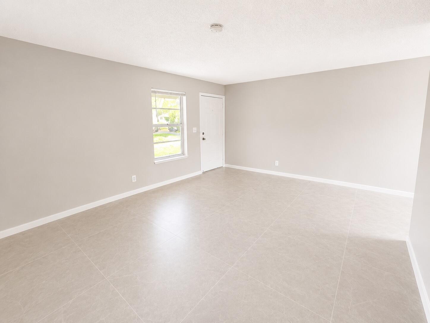 An empty room with light gray walls, large floor tiles, a window, and a door — 1794 Juno Road # 2, North Palm Beach FL 33408, NORTH PALM BEACH, FL