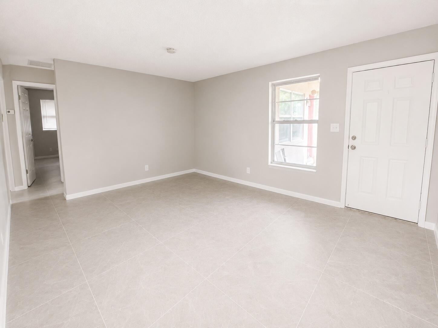 An empty room with light gray walls, large floor tiles, a window, and a door — 1794 Juno Road # 2, North Palm Beach FL 33408, NORTH PALM BEACH, FL