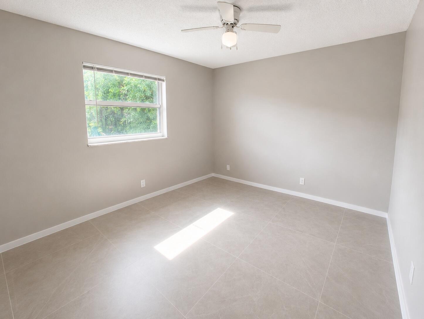 An empty bedroom features light gray walls, large neutral floor tiles, and a ceiling fan — 1794 Juno Road # 2, North Palm Beach FL 33408, NORTH PALM BEACH, FL