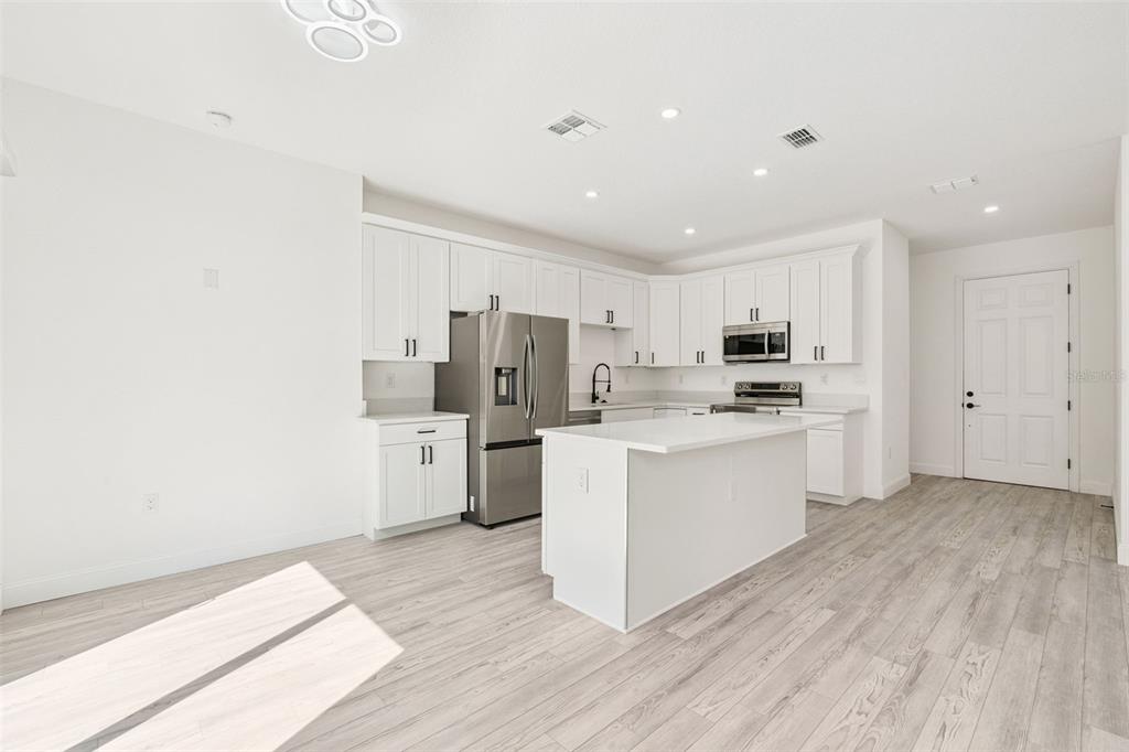 A modern kitchen features white cabinetry, stainless steel appliances, a center island, and light flooring — 7834 TERN DRIVE, ORLANDO, FL