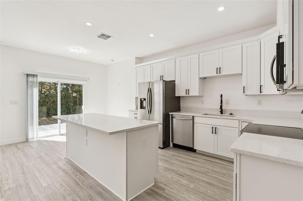 A bright, open-concept living room and kitchen featuring white cabinetry and modern furniture — 7834 TERN DRIVE, ORLANDO, FL