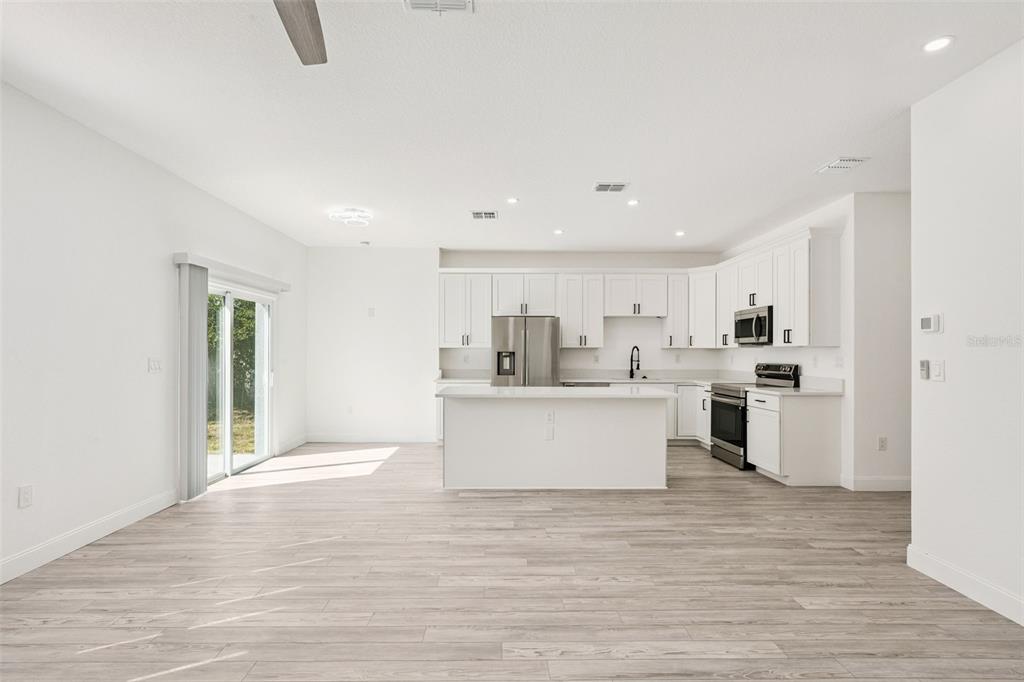 A modern kitchen and living area with white cabinets, stainless steel appliances, and wood-look flooring — 7834 TERN DRIVE, ORLANDO, FL