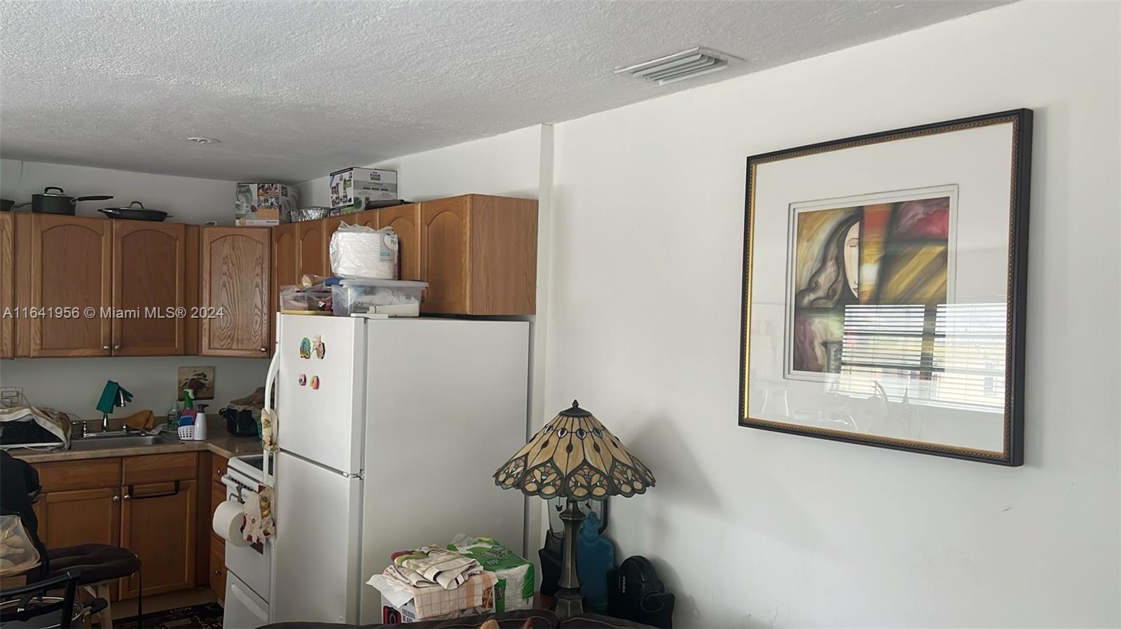A kitchen features wooden cabinets, a white refrigerator, and a framed painting on the wall — 7304 SW 82nd St # A210, Miami FL 33143, MIAMI, FL