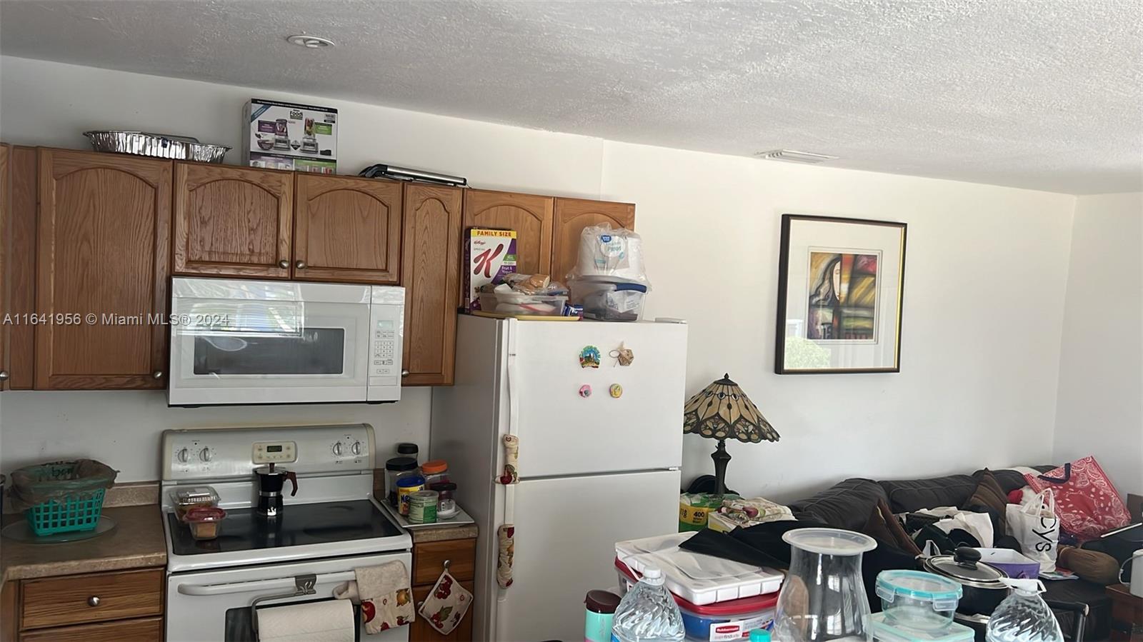 A kitchen features wood cabinets, a white stove, a refrigerator, and an adjacent living area — 7304 SW 82nd St # A210, Miami FL 33143, MIAMI, FL