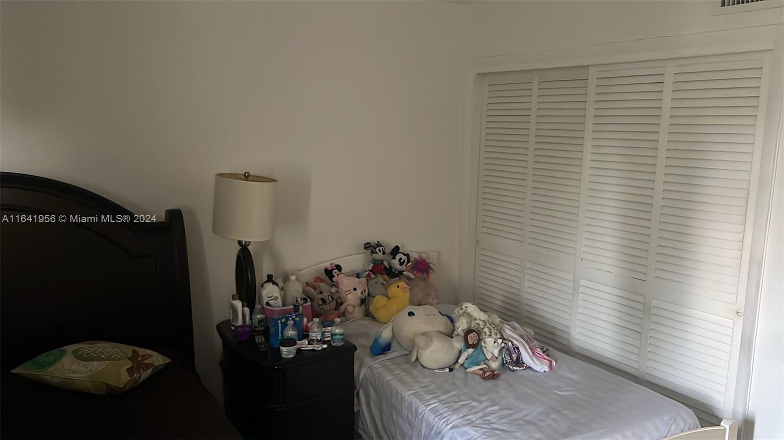 A bedroom features a bed, a nightstand with a lamp, and white louvered closet doors — 7304 SW 82nd St # A210, Miami FL 33143, MIAMI, FL