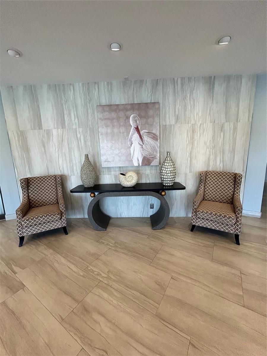 A console table with two patterned armchairs sits against a wood-look tiled accent wall — 1200 Hibiscus Avenue # 702, Pompano Beach FL 33062, POMPANO BEACH, FL