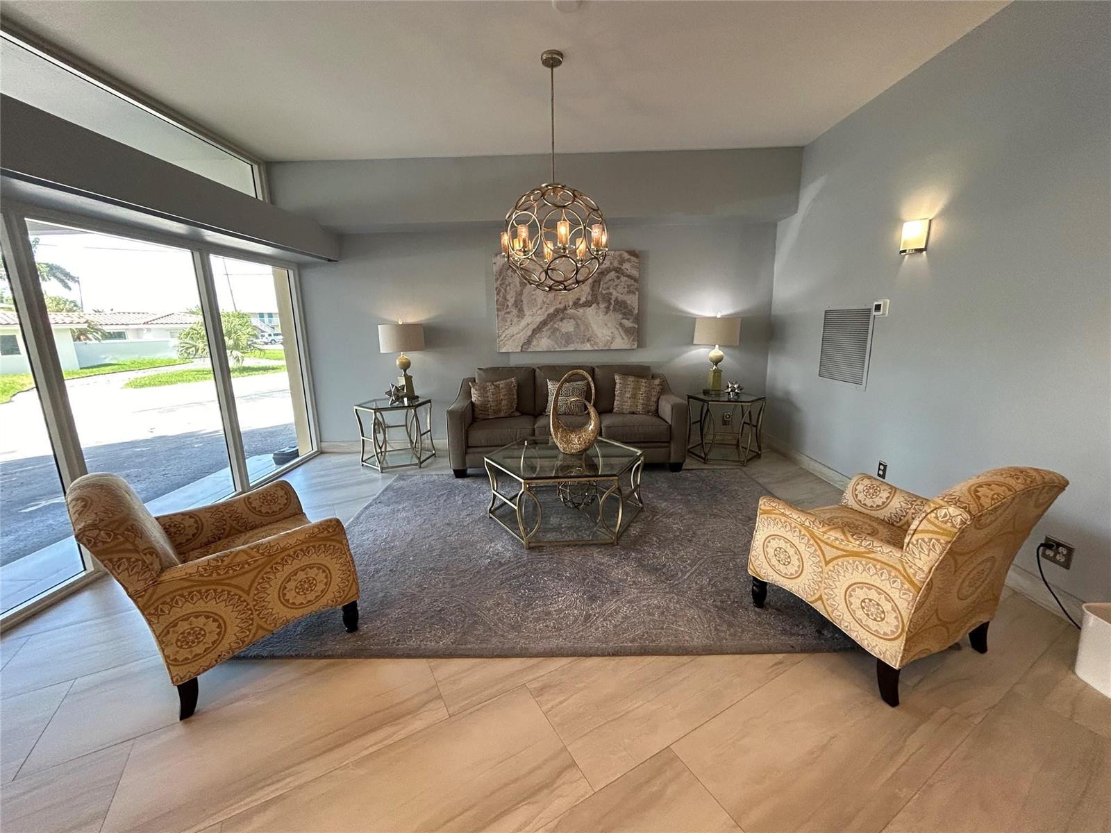 A living room features a sofa, two patterned armchairs, a glass coffee table, and chandelier — 1200 Hibiscus Avenue # 702, Pompano Beach FL 33062, POMPANO BEACH, FL