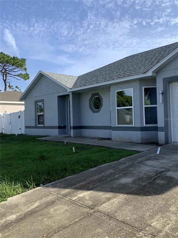 The exterior of a single-story gray house features a concrete driveway and a small lawn — 11217 ROMAN STREET, SPRING HILL, FL
